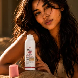 A woman with glowing skin and long dark hair poses in warm golden-hour lighting while holding EltaMD UV Clear SPF 46 sunscreen, creating a premium skincare advertisement with a natural sun-kissed aesthetic.
